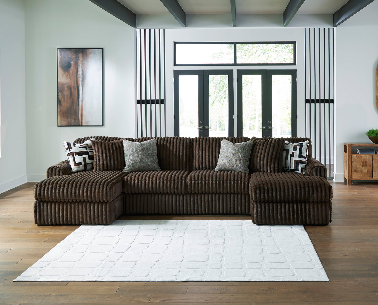 Brown sectional sofa in a living room with large windows and a rug.