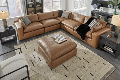 Brown leather sectional sofa with ottoman in a living room setting.