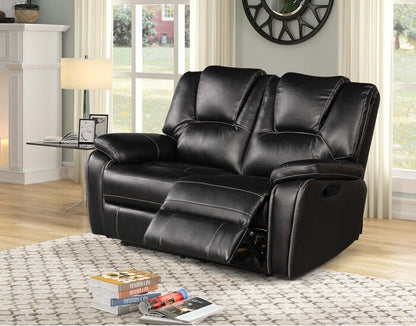 Black leather reclining Love Seat in a living room setting with books and a remote control on a rug.