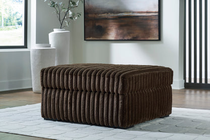 Brown textured ottoman in a living room setting with a painting and vase in the background.